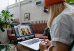 A woman wearing an orange beanie works on a digital design project on a laptop.