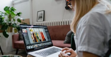 A woman wearing an orange beanie works on a digital design project on a laptop.