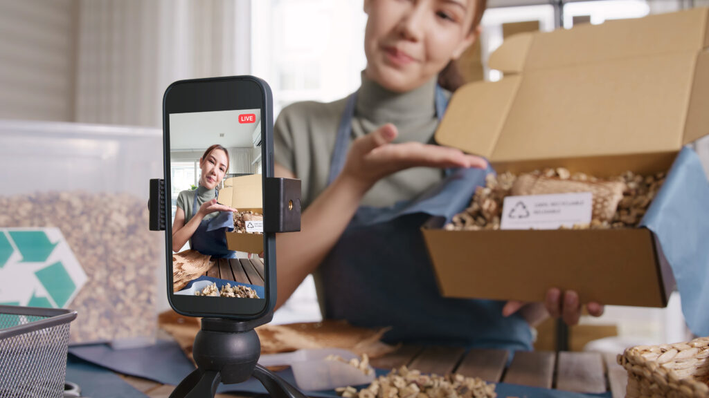 SME owner filming a social media video on her phone, recording herself opening a box.