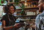 Smiling wait staff taking payment from a customer in a cafe.