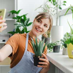 Florist taking a selfie while holding a succulent plant, surrounded by various plants