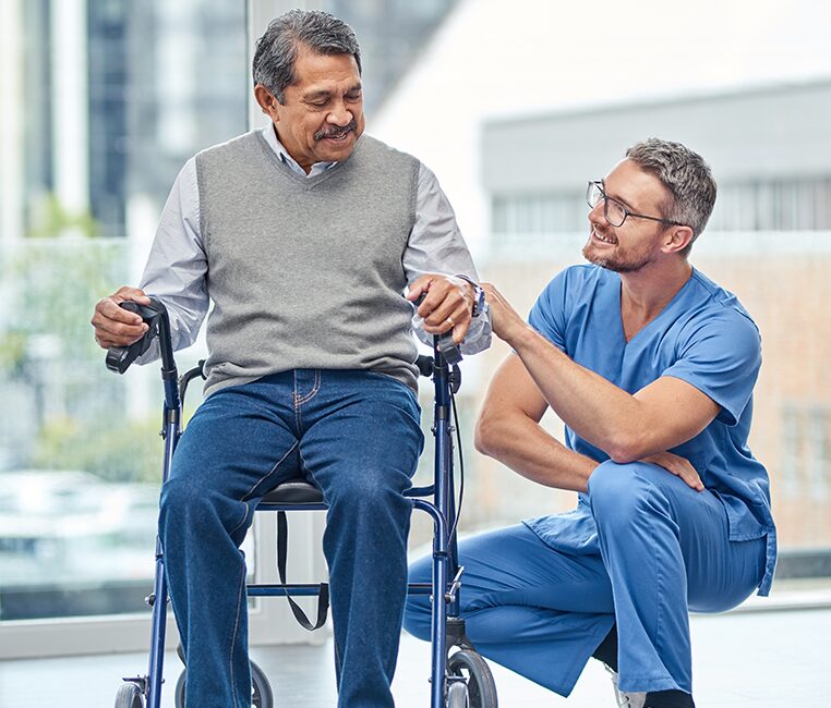 An elderly man in a wheelchair receives assistance from a disability support worker